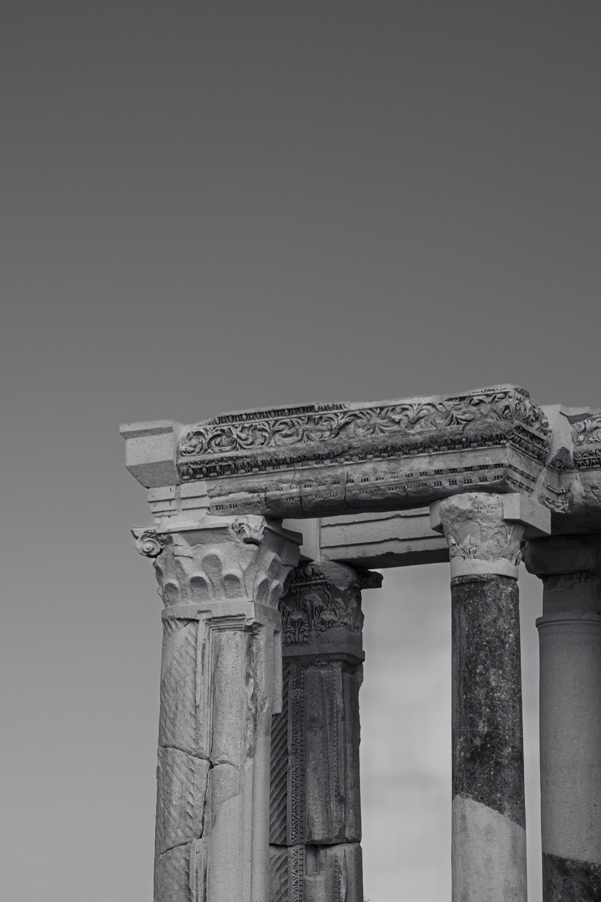 Weathered column capitals against an open sky, in black and white