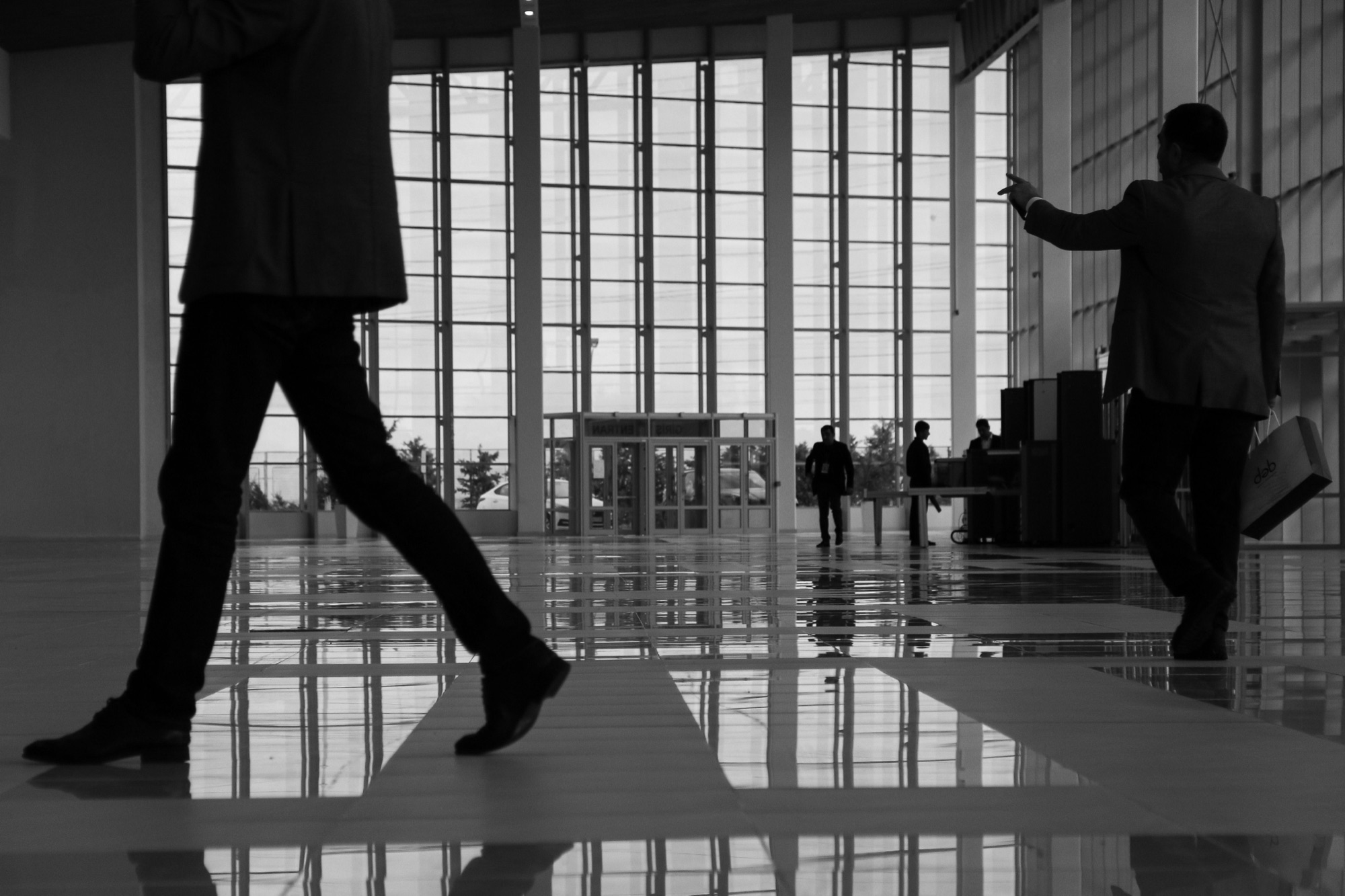 Silhouettes of people crossing a bright modern lobby, in black and white